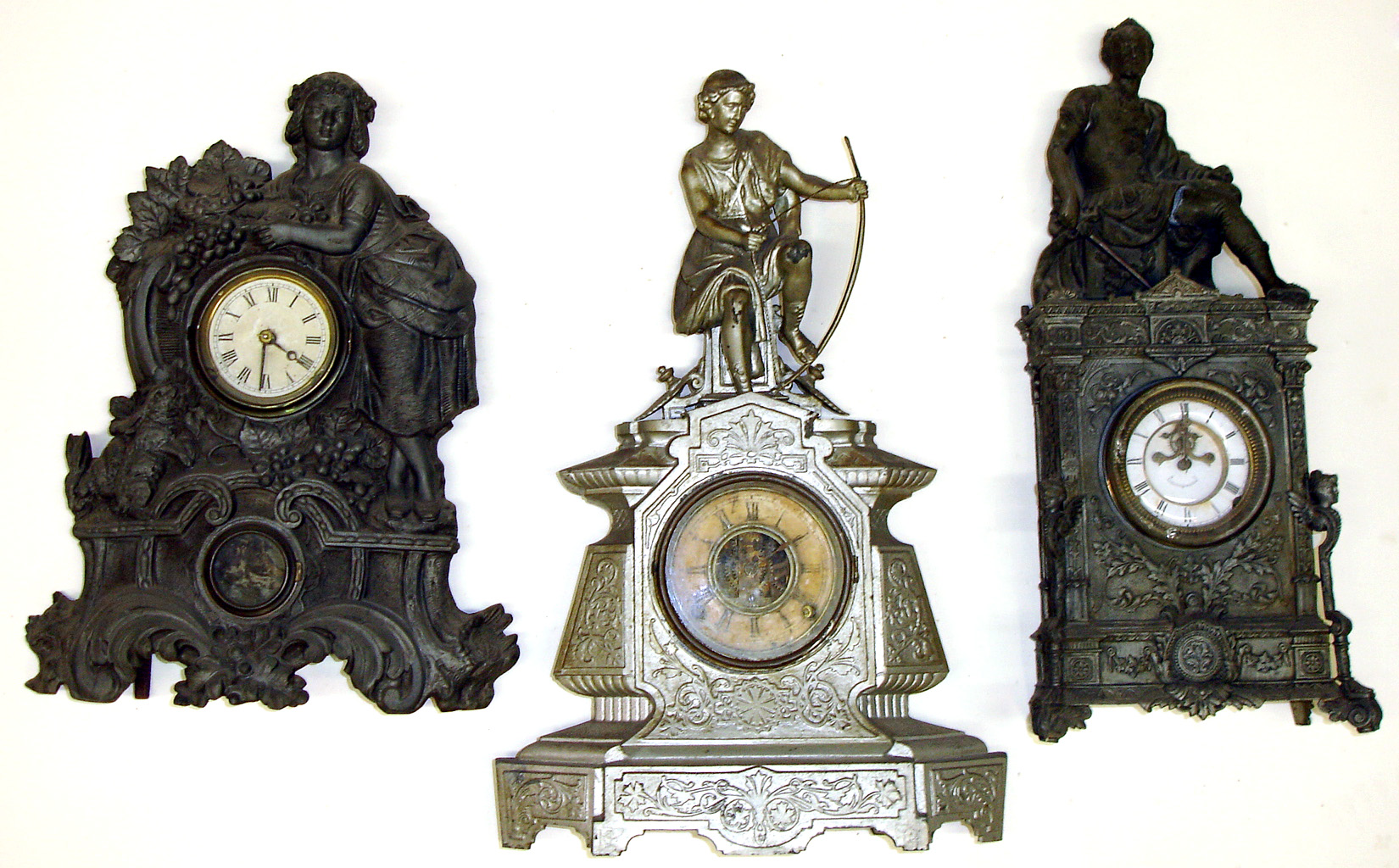 Three Connecticut 8 day cast metal and wood figural mantel clocks- there are two seated men with weapons and a Muller No. 67 with a standing peasant woman with fruit and rabbits, tallest is 23" high — Antique Clocks Price Guide