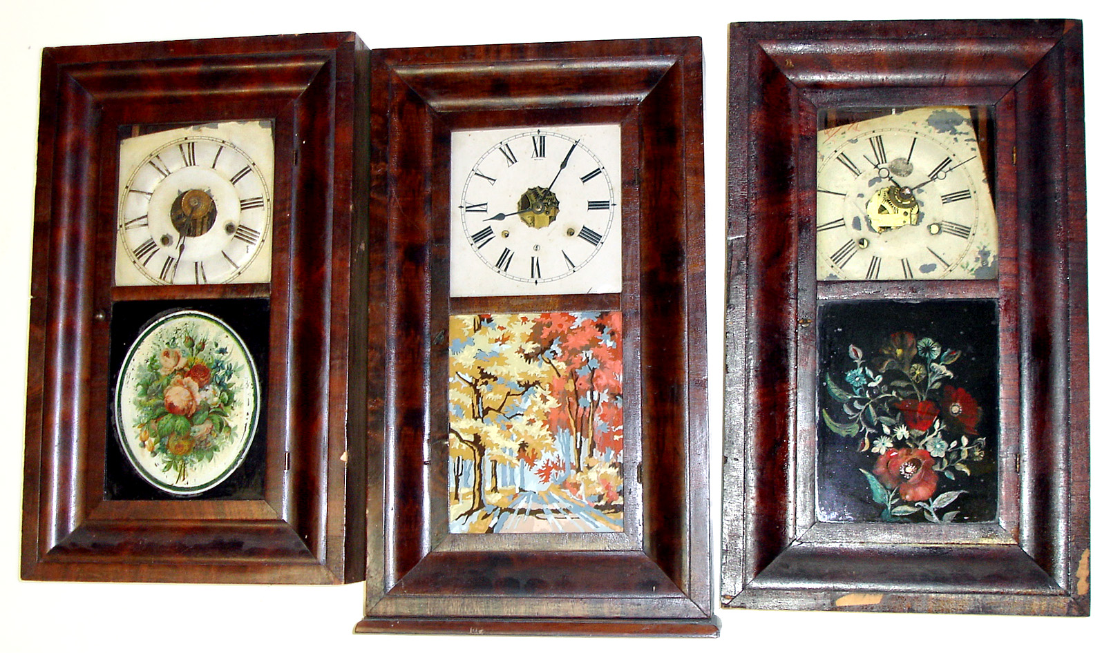 Three ogee 30 hour weight driven shelf clocks- an Ansonia Brass and Copper with colorful later painted glass of autumn foliage, a Seth Thomas with early oval floral glass and an E. and A. Ingraham (Waterbury movement) with later but well done floral tablet. Tallest, with extra bottom molding, is 27" high — Antique Clocks Price Guide