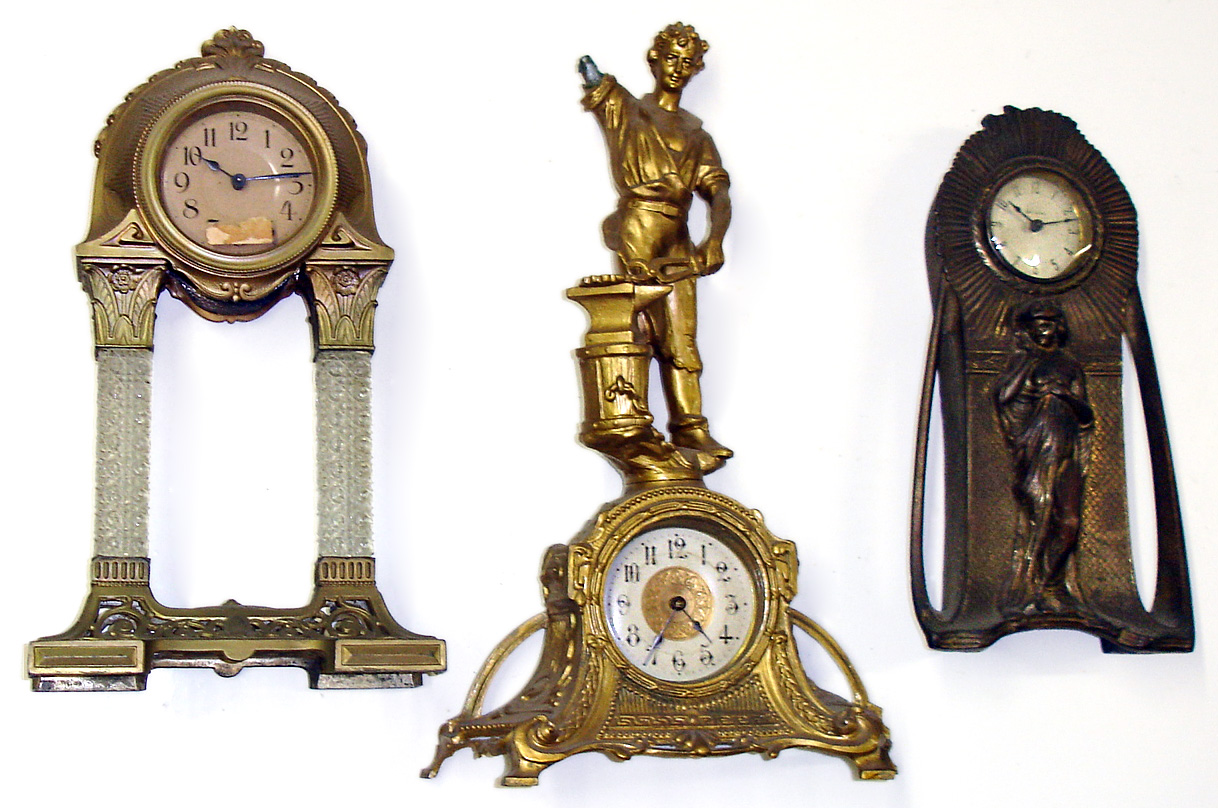 Three large cast metal American novelty clocks. Rear wind pin pallet movements. Shortest Nouveau style is a New Haven. Middle has nice square glass columns. Tallest, in gold finish, of blacksmith (missing arm) is 18" high. — Antique Clocks Price Guide