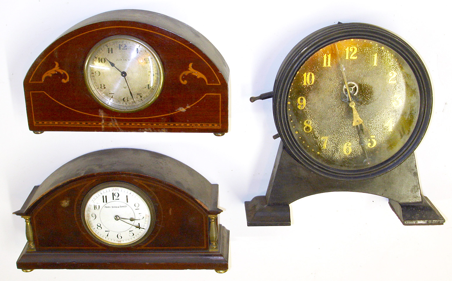 Three quality European desk clocks. Two are nice inlaid solid wood cases and balance wheel 8 day time only movements; one Swiss, one English with walking lion trademark and Henry Birks and Sons enamel dial. Third is British novelty with barbell pendulum, visible escapement and interior weight lifted by side lever, 10.5" high. — Antique Clocks Price Guide