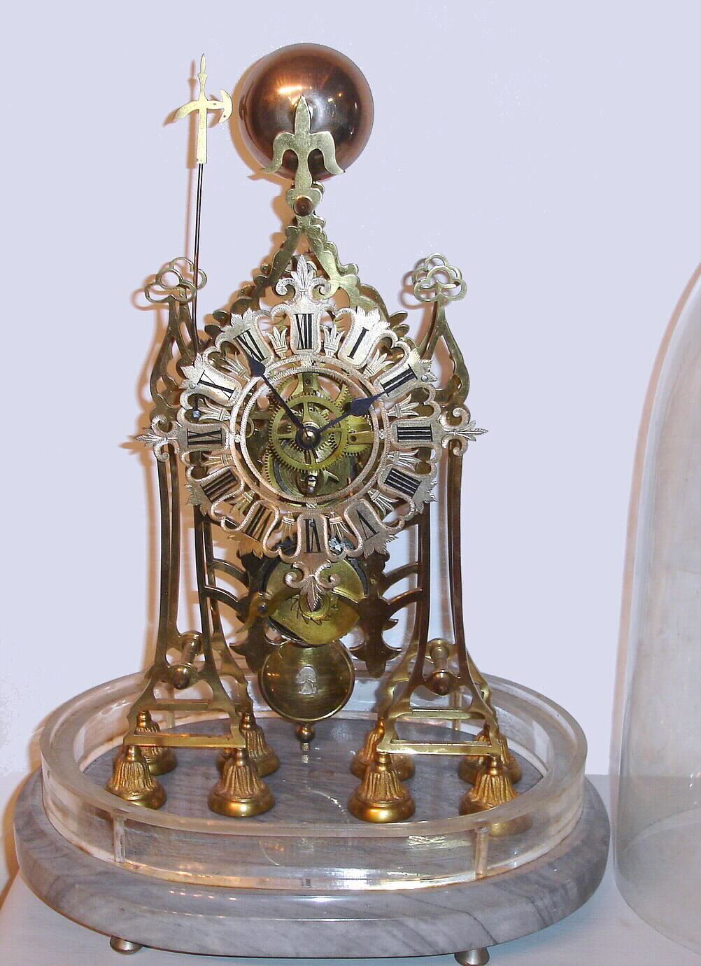 English, Single Fusee skeleton clock with anchor escapement and single passing strike at the hour, the frame resting on 8 cast round feet mounted to a gray marble base, with a 2" plexi-glass spacer added to allow the old glass dome to clear the clock and hammer when striking. — Antique Clocks Price Guide