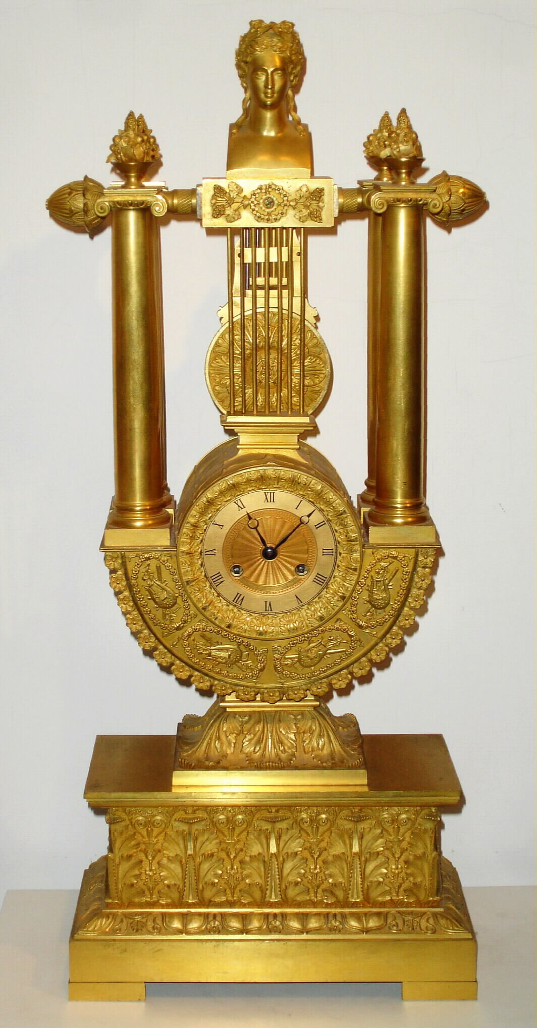 French, Empire style lyre mantel clock, with knife edge suspension of pendulum above the dial, 8 day spring, movement numbered 210. The case profusely decorated with acanthus leaves, pineapples to the right and left of the top, and each column surmounted by a small urn with floral display, c1830 — Antique Clocks Price Guide
