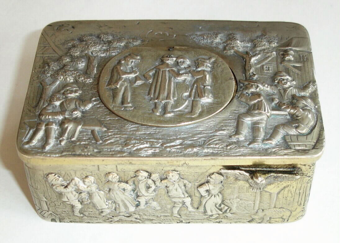 Swiss, Singing Bird Box, an embossed silver case featuring village scenes of people in period costumes, some dancing, some in a musical group, others sitting, holding hands, even the very bottom panel includes a couple dancing on the beach, with a pipe smoking on-looker. A hinged snuff box lid in the rear shows a farmer's wife milking a cow, and sheep in the field, c1925 — Antique Clocks Price Guide