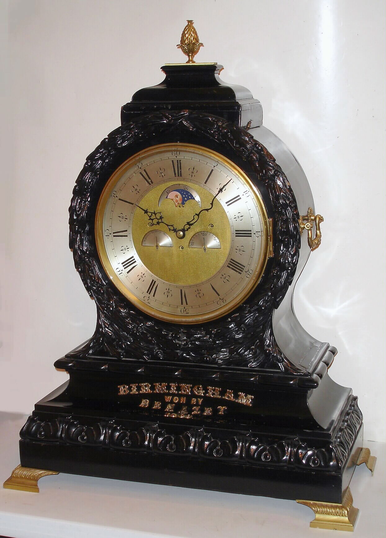 English, J. C. Jennens, London, giant triple fusee bracket clock, quarter chiming, a race award presented to owners of "Benazit", and with large brass letters screwed the base = "Birmingham, Won By Benazit, 1869". With a very large and robust movement, with round silvered dial containing in its center a Halifax rolling moon, days of the week dial to left and a simple calendar dial (1-31) to the right. Playing the Westminster tune on 4 large and deep toned bells, and striking the hours on an extra large cathedral gong. The balloon shaped case with floral carving to the front, c1869 — Antique Clocks Price Guide