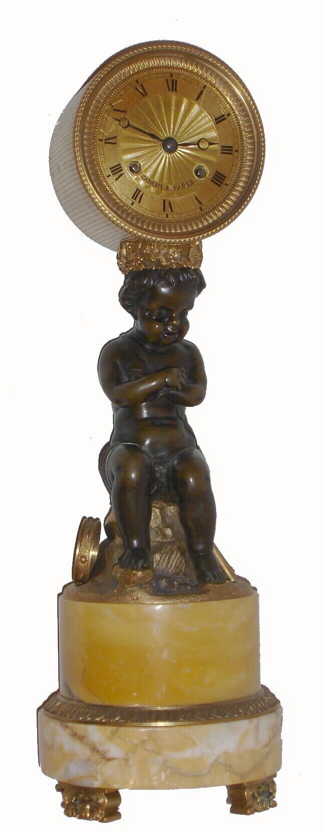 French, Canchy, a Paris, a bronze and marble mantel clock, slender in nature, with a finely finished seated cherub, a tambourine at his feet and arms folded, surmounted by a fluted brass canister containing a well made bell strike movement with 60-pin escape wheel and silk thread suspension. C.1825. — Antique Clocks Price Guide