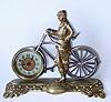 English, British United Clock Co, Ltd, Birmingham, a cast brass bicycle and male rider, in period riding clothes, and with a 30 hour rear wind and set movement in place of the front wheel, the whole on a shaped brass base with a cartouche bearing the initial "S", c1910