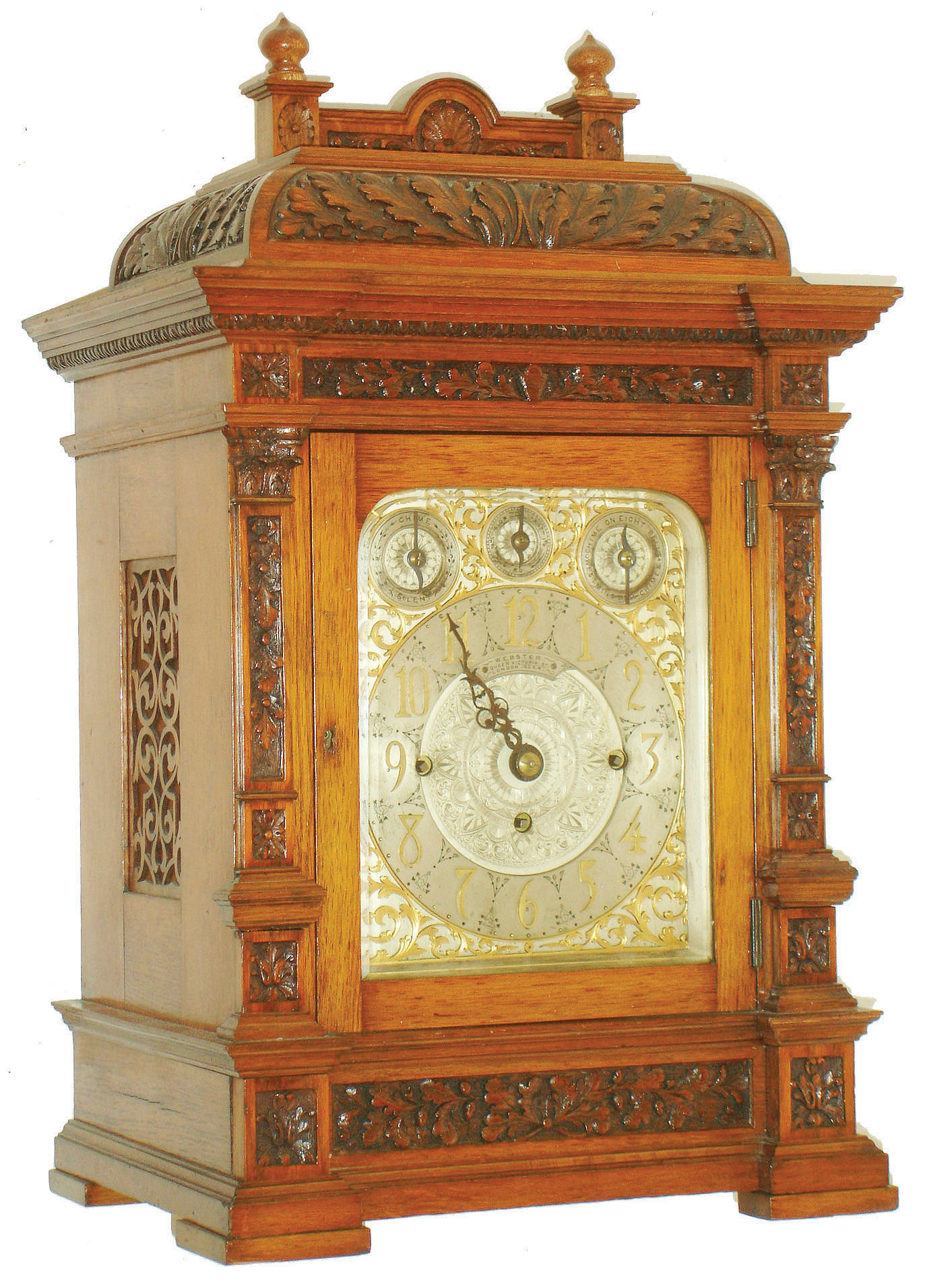 Webster, Queen Victoria St., London, large bracket clock with chiming on choice of bells or gongs, oak case with carved panels featuring oak leaves and acorns at the base, frieze, and top, front door with thick beveled glass, flanked by carved pilasters with Corinthian capitals, molded cornice with egg and dart molding, the case top finished with two capped plinths with carved paterae and topped with finials, solid balustrade with central arch carved with a scallop shell and lateral foliage, case sides with pierced wooden fret with fabric backing, and back door with brass lattice fret with fabric backing, beautiful composite dial with silvered ground, gilt, pierced flowing acanthus dial mask with engraved detail, silvered applied chapter ring with gilt Arabic numerals, dial center engraved with acanthus and Aesthetic motifs, top of dial with strike/ silent indicator, regulation dial, and chime selector, pierced, blued steel hands, very heavy, unsigned, fusee movement, chiming the quarters on bells (Whittington) or gongs (Westminster), and with large gong for counting the hours, original key, c1880 — Antique Clocks Price Guide