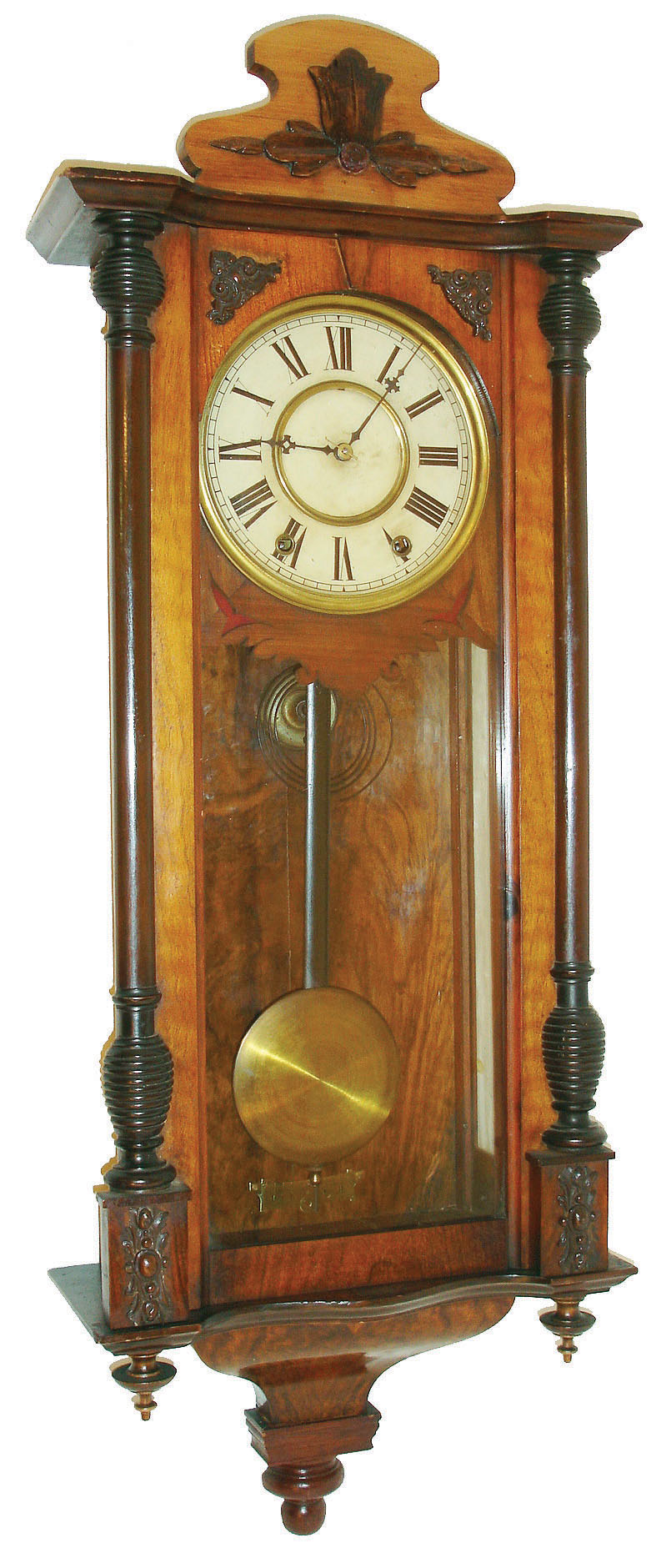 New Haven Clock Co., New Haven, Conn., Vienna regulator style wall clock, walnut case with glazed door and sides, door with turned half columns with ribbed capitals and bases, applied composition ornament, case top piece with applied carving, the base with walnut veneered, deeply molded ogee bracket with central drop, Roman numeral white painted metal dial fixed to a walnut veneered frame with fretwork lower edge, and with fabric backed cutouts below 5:00 and 7:00, blued steel hands, 8 day time and strike movement, c1880 — Antique Clocks Price Guide