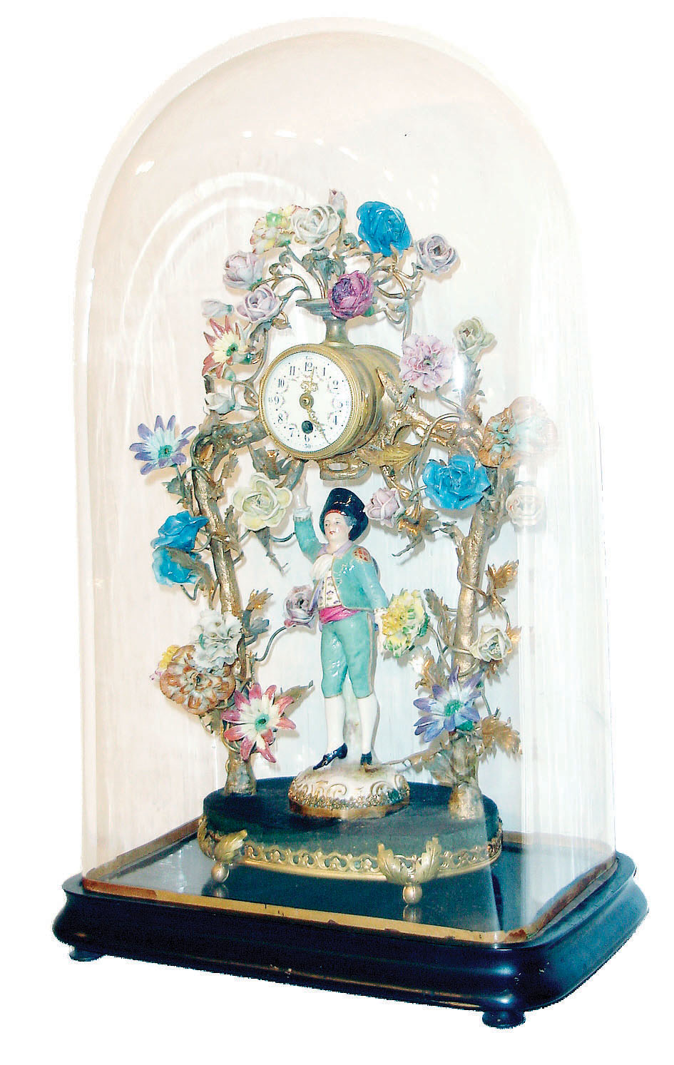 Boler, France, porcelain and gilt brass clock, the base with dark finish, and trimmed with gilt ornament, with figure of a young man, colorfully dressed in the 18th century style, and with a lute slung over his back, standing below gilt trees covered with multi colored flowers of diverse size and shape, and supporting a gilt case containing a French 8 day time only movement,  Arabic numeral white enamel dial with floral garlands, and gilt Louis XV style hands, base with tag marked "Made in France Boler 27 Rue S Honore", all under a glass dome on an ebonized wooden base, c1900 — Antique Clocks Price Guide
