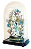 Boler, France, porcelain and gilt brass clock, the base with dark finish, and trimmed with gilt ornament, with figure of a young man, colorfully dressed in the 18th century style, and with a lute slung over his back, standing below gilt trees covered with multi colored flowers of diverse size and shape, and supporting a gilt case containing a French 8 day time only movement,  Arabic numeral white enamel dial with floral garlands, and gilt Louis XV style hands, base with tag marked "Made in France Boler 27 Rue S Honore", all under a glass dome on an ebonized wooden base, c1900