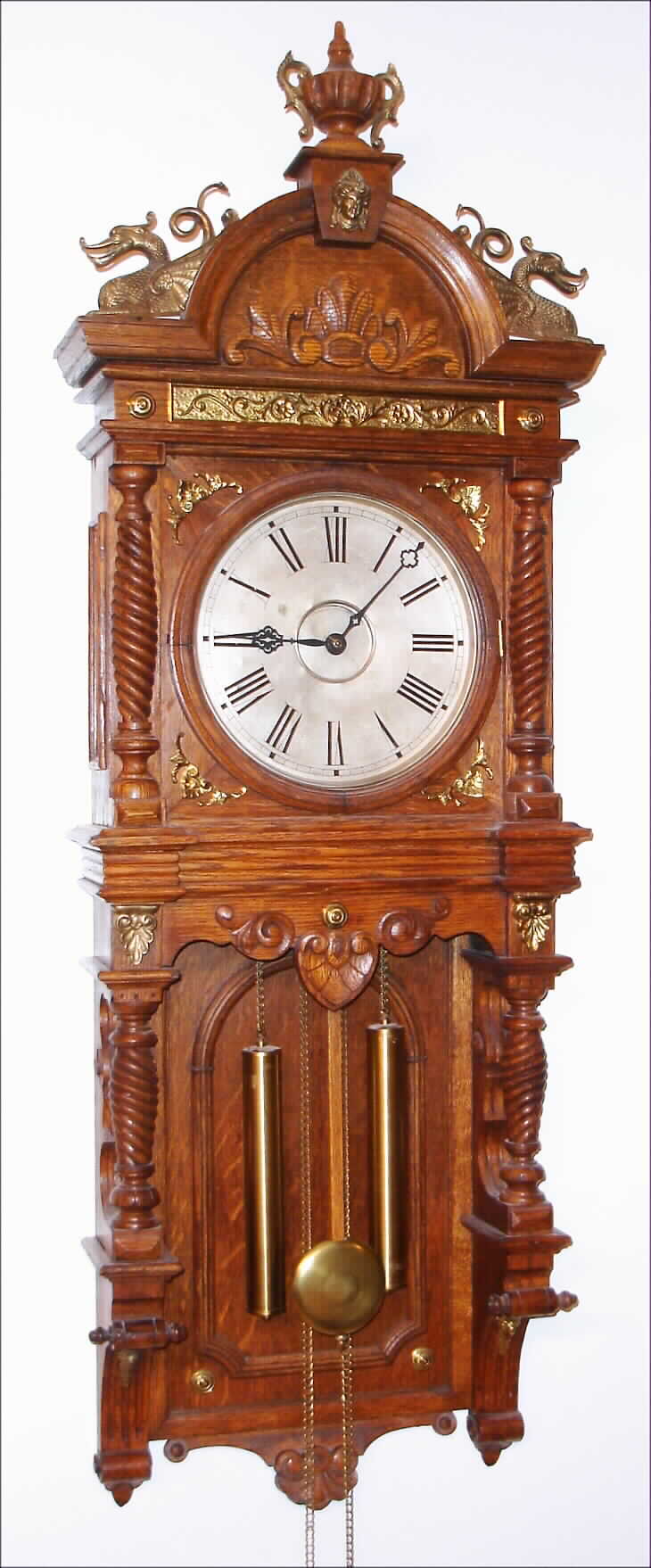 Waterbury Clock Co., Waterbury, Conn., "Augusta" wall clock, 8 day, time and strike, two weight driven movement in an oak case with cast brass ornaments and silvered metal dial, c1893 — Antique Clocks Price Guide