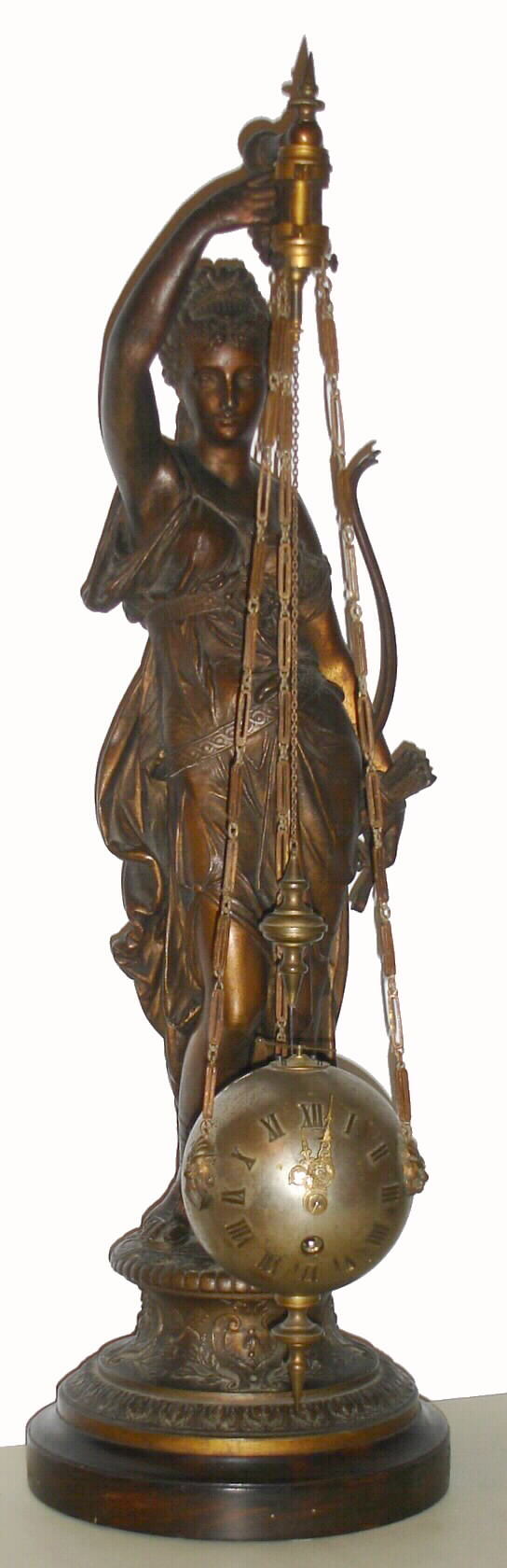 French conical pendulum clock, the spherical clock suspended on chains, held aloft by a patinated spelter statue of Diana, the figure resting on a decorative cast plinth, attached to a turned wooden base, eight day spring driven time only movement, case with silvered finish, applied gilt brass Roman numerals, fancy gilt hands, lions head mounts for chains, arrow form crutch at top of sphere, gilt brass suspension with four steel springs, c1890 — Antique Clocks Price Guide
