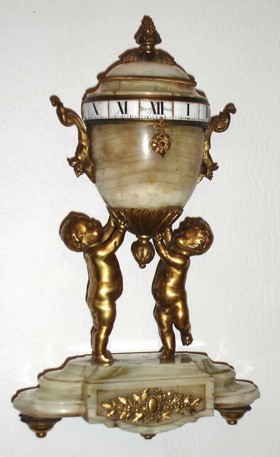 Tiffany and Co., New York, French miniature urn form desk clock with annular dial, time only, spring driven eight day movement with lever platform escapement, the annular dial with Roman numeral white enamel plaques set in a gilt brass ring, signed Tiffany and Co., New York at 12:00, fleur de lis form indicator for time, the polished agate urn with gilt handles, supported by two wingless cherubs, polished agate base decorated with gilt brass laurel appliques on gilt toupie feet, c1890 — Antique Clocks Price Guide
