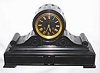 Tiffany and Co., New York, French black slate Drumhead style mantel clock, spring powered eight day time and strike movement signed Tiffany and Comp., striking the hours and half hours on a bell, fluted cylindrical case supported by scrolls on a molded rectangular base, decorated with shallow carving, the scrolls with volutes, gilt bezel with beveled glass, black slate dial with engraved Roman numerals finished with gold, polished brass hands, c1880