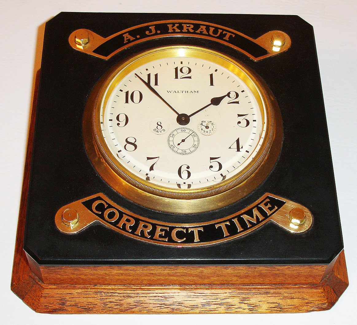 American Waltham Watch Co, Waltham, Mass., eight day time only car clock with up/ down indicator in a purpose made mahogany case, top of case finished with a black plate, possibly Bakelite mounted with brass plates embossed "A. J. Kraut" and  "Correct Time", inside if case back stamped 173, brass carrying handle mounted to case side above 12, matte silvered Arabic numeral dial with seconds, signed Waltham, brass bezel with beveled glass, blued steel hands, c1920 — Antique Clocks Price Guide