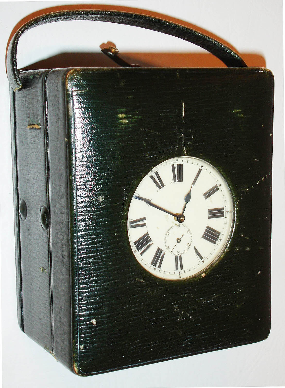 England?, leather bound travelling clock with Swiss thirty hour watch movement, pin pallet escapement, celluloid Roman numeral dial, backlit for viewing at night by depressing button on top of case, green velvet lining and key holder in front compartment, back compartment with battery holder, blued steel hands, c1910 — Antique Clocks Price Guide