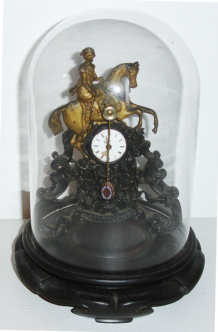Austria, thirty hour Zappler clock for the English market, white enamel Roman numeral dial, gilt hands, decorative pendulum, cast iron case with Queen Victoria on horseback, the lower section with rococo ornament, a crown, and embossed at the bottom Victoria 1, mounted to a wooden base, under a glass dome c1850 — Antique Clocks Price Guide