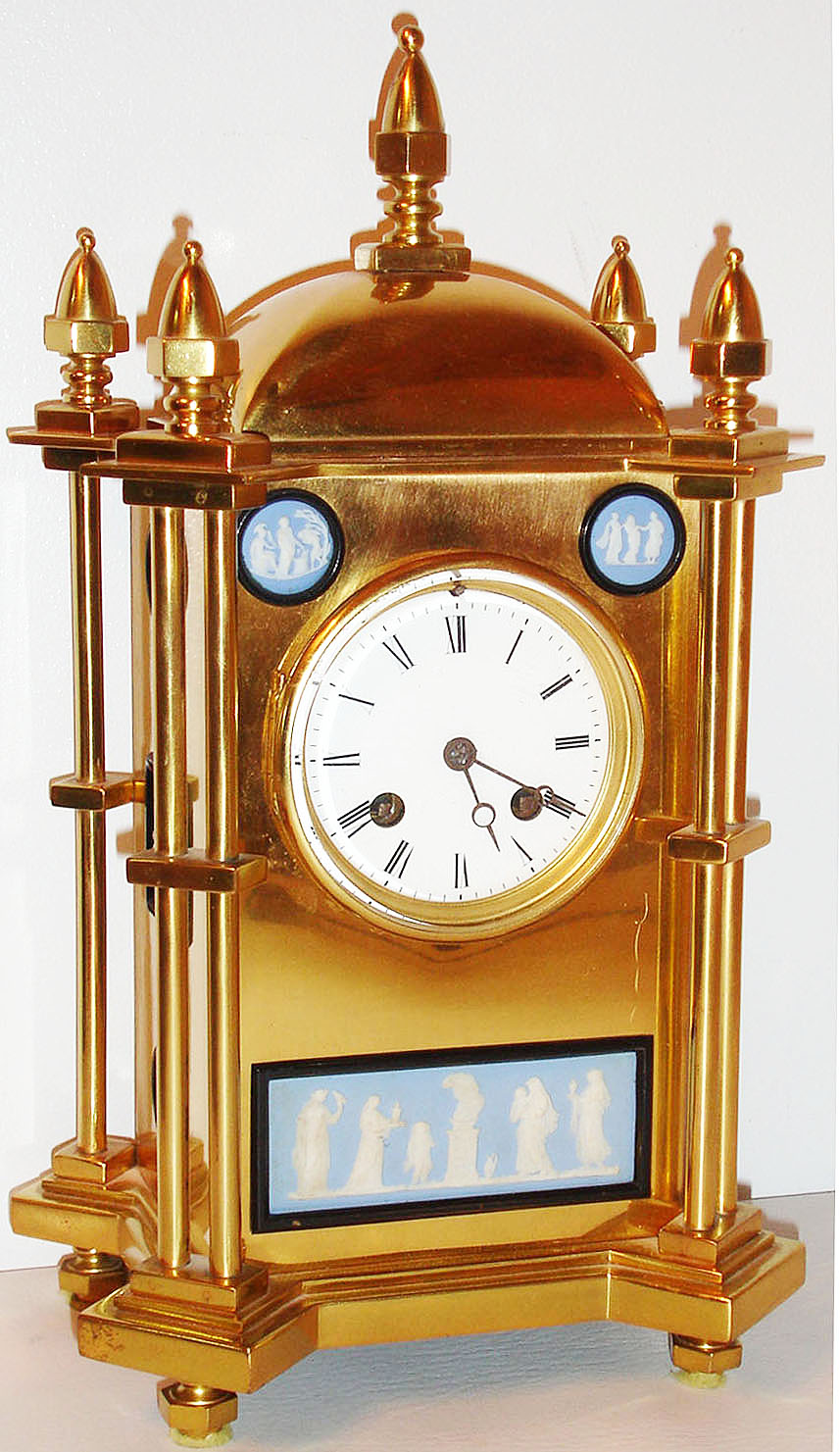 France, probably for the English market, a brass Gothic style mantel clock set with signed Wedgwood plaques, Japy Freres eight day time and strike movement, white enamel Roman numeral dial, Breguet style hands, bezel with beveled glass, polished brass case with columned corners, topped by acorn form finials, set with blue jasper plaques decorated with classical and allegorical motifs, each set in its own black painted, metal frame c1860 — Antique Clocks Price Guide
