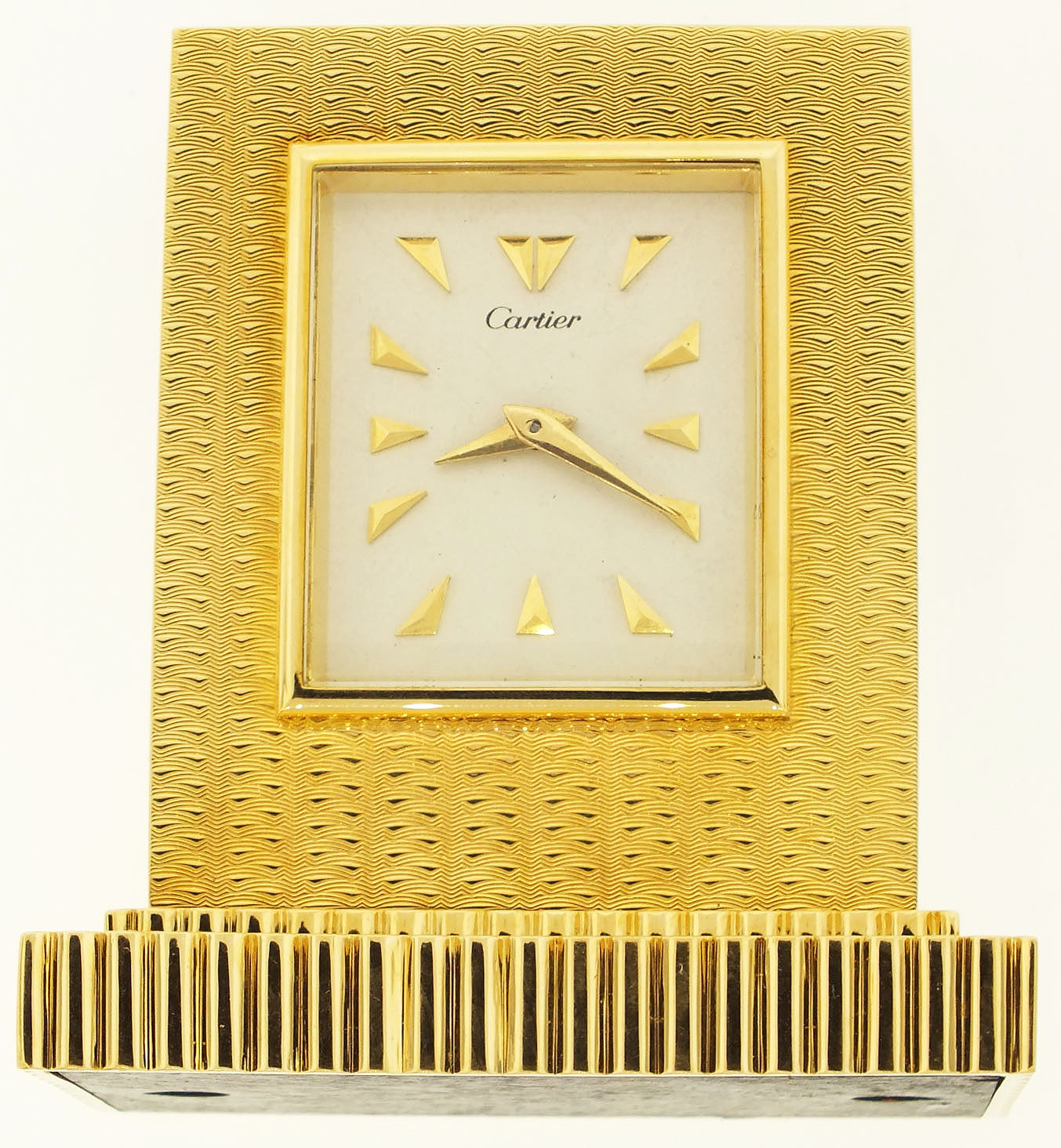Cartier, Paris, France, small desk or nightstand clock, 15 jewels, key wind and set, gilt plate movement, with lever escapement, in an 18 karat, yellow gold, straight line engine decorated case, and silver dial with gold pyramid markers, gold dauphine hands, serial #658, 341.9g TW c1975, with original key, L 2 1/2" W 1 5/8" Ht 2 3/4" — Antique Clocks Price Guide