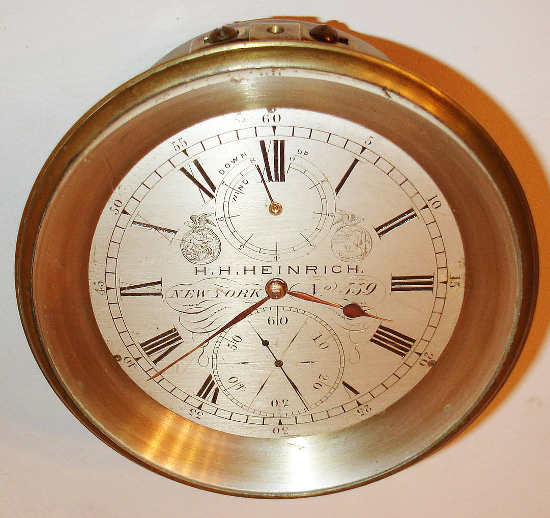 H. H. Heinrich, New York, marine chronometer of eight day duration, the movement with gilt plates, blued steel screws, spring detent escapement, cut bimetallic balance with cylindrical weights for temperature compensation, blued steel helical balance spring, diamond end stone in blued setting, the escapement, third, and fourth wheels mounted as a sub assembly which can be removed without complete disassembly of the movement, brass bezel with beveled glass, silvered Roman numeral dial with black outer 5 minute markers, wind indicator, engraved with makers name and location, and No. 559,gold hands with blued steel seconds, contained in a heavy brass tub marked with owners name H. A. Urnhammer, with key, c1890 — Antique Clocks Price Guide
