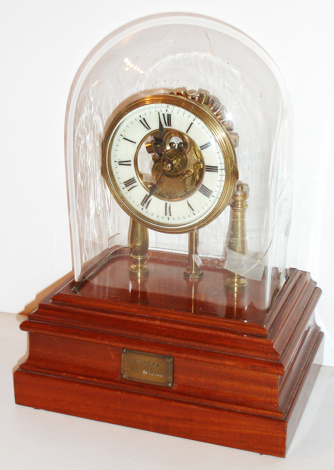 Eureka Clock Co., Ltd, London, England, the "1000 day" battery powered movement with large bimetallic balance and spotted brass plates, supported by two turned baluster form columns, with white enamel Roman numeral dial, blued steel spade hands, brass bezel with convex beveled glass, all covered with a glass dome, and mounted to a beautifully made, polished mahogany base with battery compartment, the front with a brass plaque engraved "Eureka 1000 Day Motion" c1910 — Antique Clocks Price Guide
