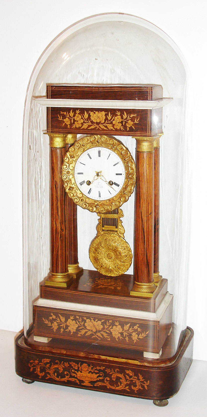French portico clock with base and dome, 8 day, time and strike, pendule a Paris movement, recoil escapement and count wheel striking on a bell, white enamel Roman numeral dial, with unusual dedication in enamel, "For Vito Viti", fancy gilt hands, gilt brass gridiron style pendulum ornamented with dolphins, flowers and foliage, Brazilian rosewood veneered case with marquetry, the base also with rosewood veneer and light wood marquetry, with gilt bronze bezel, column capitals and bases, white painted moldings and feet, under a glass dome, c1840 — Antique Clocks Price Guide