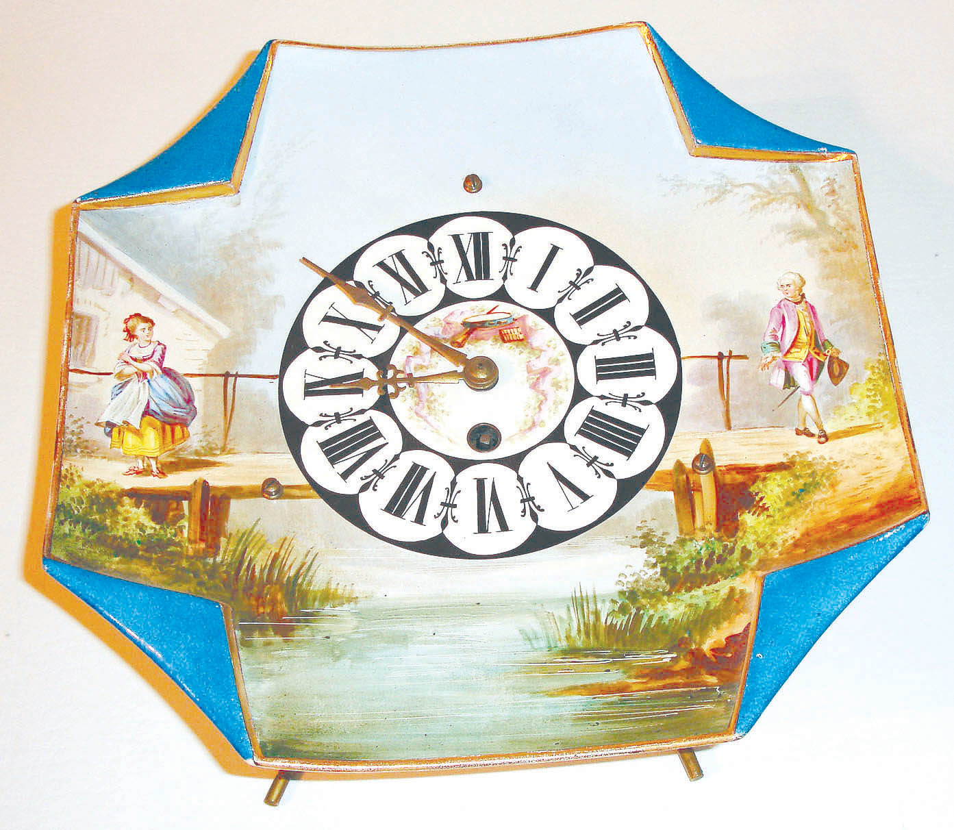 France or Germany, earthenware plate clock with easel back, square, gilt edge with folded corners, with a rural scene in polychrome over glaze enamels, featuring a man and a woman on opposite sides of a bridge, each dressed in 18th century style clothing, Roman numeral dial with brass hands, the dial center decorated with a small trophy featuring musical instruments 8 day, time only, pendulum movement with tic tac escapement, c1900 — Antique Clocks Price Guide