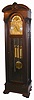Colonial Mfg. Co., Zeeland, Michigan, Model No. 1211, 9-tube hall clock, 8 day, time, strike and chime, three weight driven European movement playing Whittington, Westminster or Canterbury tune in maple case stained dark walnut with ornately carved full length Corinthian columns, well carved bracket feet and crest, beveled glass sides and locking beveled glass side doors accessing movement. The brass arched dial has a silvered chapter ring with applied brass numerals, cast spandrels and dial center, rolling moon phases  in arch, selection for tunes or silent, and second's bit, c1930