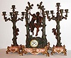 French figural garniture with candelabra, with 8 day pendule a Paris time and strike movement, recoil escapement and count wheel striking on a bell, white enamel Arabic numeral dial with floral decoration, blued steel hands, gilt brass bezel with beveled glass, the large case of patinated spelter, with a young couple swinging between two pruned tree trunks, the trunks supporting vines with leaves and ferns below, the rustic style feet with oak leaves and acorns, on a marble base with fine red orange veining, and set with a small plaque engraved "Idylle Printaniere Par Geo. Maxime", the right side of the clock case also signed Geo. Maxime, the candelabra also with pruned trunks supporting vines, each with a single Putti, ending in spreading branches with leaves and budding flowers, each supporting one bud form candle cup, and supported by marble bases on 4 rustic feet, with key c1880