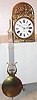 French 3 train Morbier clock, the large movement with recoil escapement, and quarter striking on 3 bells, striking the hour on a large bell, large gridiron style lyre pendulum with large convex brass shell ball, driven by three gold painted cast iron weights, white Roman numeral enamel dial marked "Procure Generale 1906", pierced brass hands,  the brass surround stamped in high relief and depicting two birds, leaves and flowers, decorated sheet iron doors on either side of the case provide access to the movement, and sheet iron back stamped with concentric squares and circles, c1906