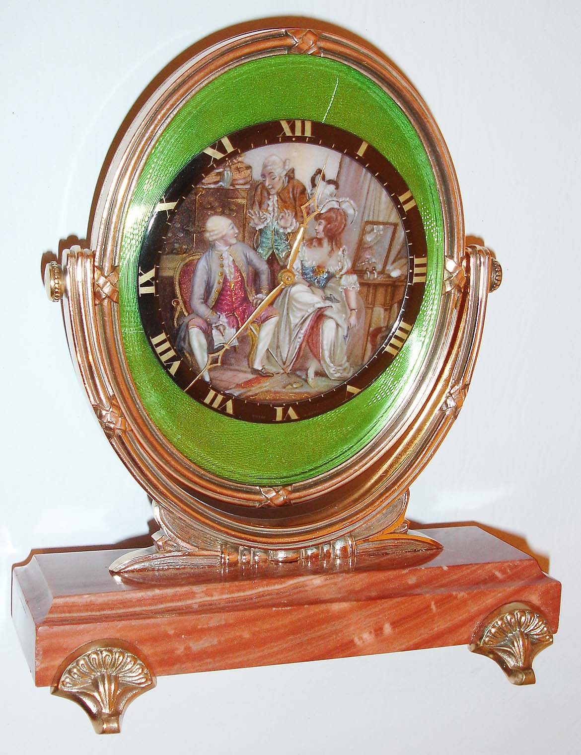 Henry Sandoz and Son Watch Co., Switzerland, 8 days, back wind and set desk or table clock mounted to a stone base on gilt feet, the clock in an gilt oval frame with pivoted support, dial center with a very colorful enamel scene featuring three figures in 18th century style attire, the woman seated before her dressing table, with one man seated and another standing, the latter engaged in conversation with the others (trying to get himself out of trouble?), framed by a black enamel chapter with gold Roman numerals, gold hands, all on a green guilloche enamel ground, and under a beveled oval glass, nickel movement with cotes de Geneve decoration, c1950 — Antique Clocks Price Guide