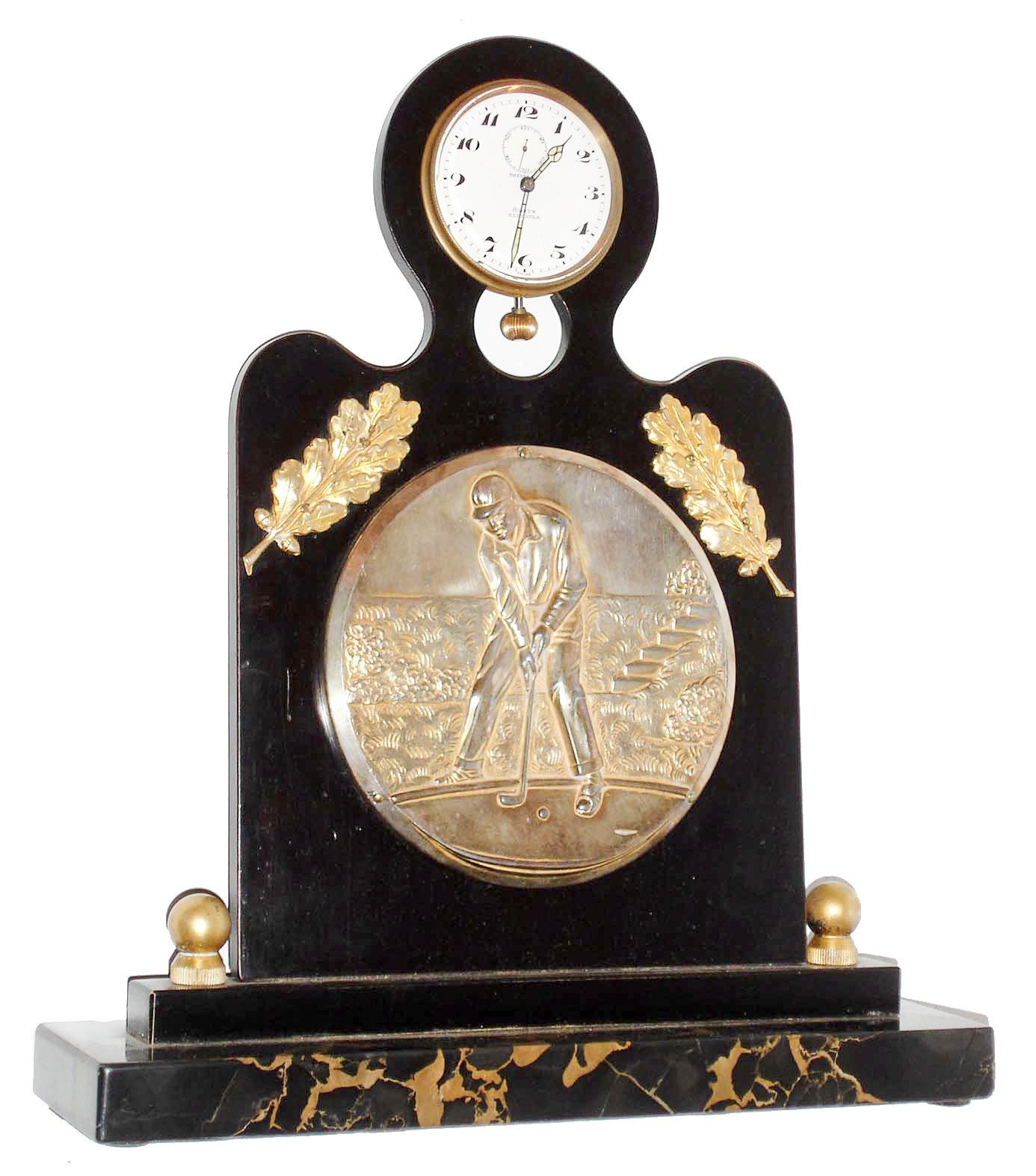 Angelus Watch Co., Switzerland, for Tiffany & Co., New York, golf themed desk clock with 8 days, minute repeating clock, the veined black marble base supporting an ebonized wood stand, mounted with a gilt repousse style plaque depicting a golfer putting, with two applied gilt branches with oak leaves above the plaque, and with clock mounted at the top, the 8 day, 15 jewel, minute repeating nickel plate movement with centrifugal governor, lever escapement with cut bimetallic balance, white enamel dial with Arabic numerals, signed "Tiffany & Co. 8 Days Repeater", with blued steel luminous hands, back of case dated May 14, 1932 — Antique Clocks Price Guide