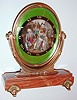 Henry Sandoz and Son Watch Co., Switzerland, 8 days, back wind and set desk or table clock mounted to a stone base on gilt feet, the clock in an gilt oval frame with pivoted support, dial center with a very colorful enamel scene featuring three figures in 18th century style attire, the woman seated before her dressing table, with one man seated and another standing, the latter engaged in conversation with the others (trying to get himself out of trouble?), framed by a black enamel chapter with gold Roman numerals, gold hands, all on a green guilloche enamel ground, and under a beveled oval glass, nickel movement with cotes de Geneve decoration, c1950