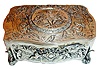 Germany, probably Karl Griesbaum, singing bird box, sterling silver, serpentine form repousse case with landscapes inhabited by putti, on scrolled acanthus form feet, the cover with figure conducting a bird and putti orchestra, the bird with red, green, and black feathers emerges and does his routine when the start slide is pushed, c1950