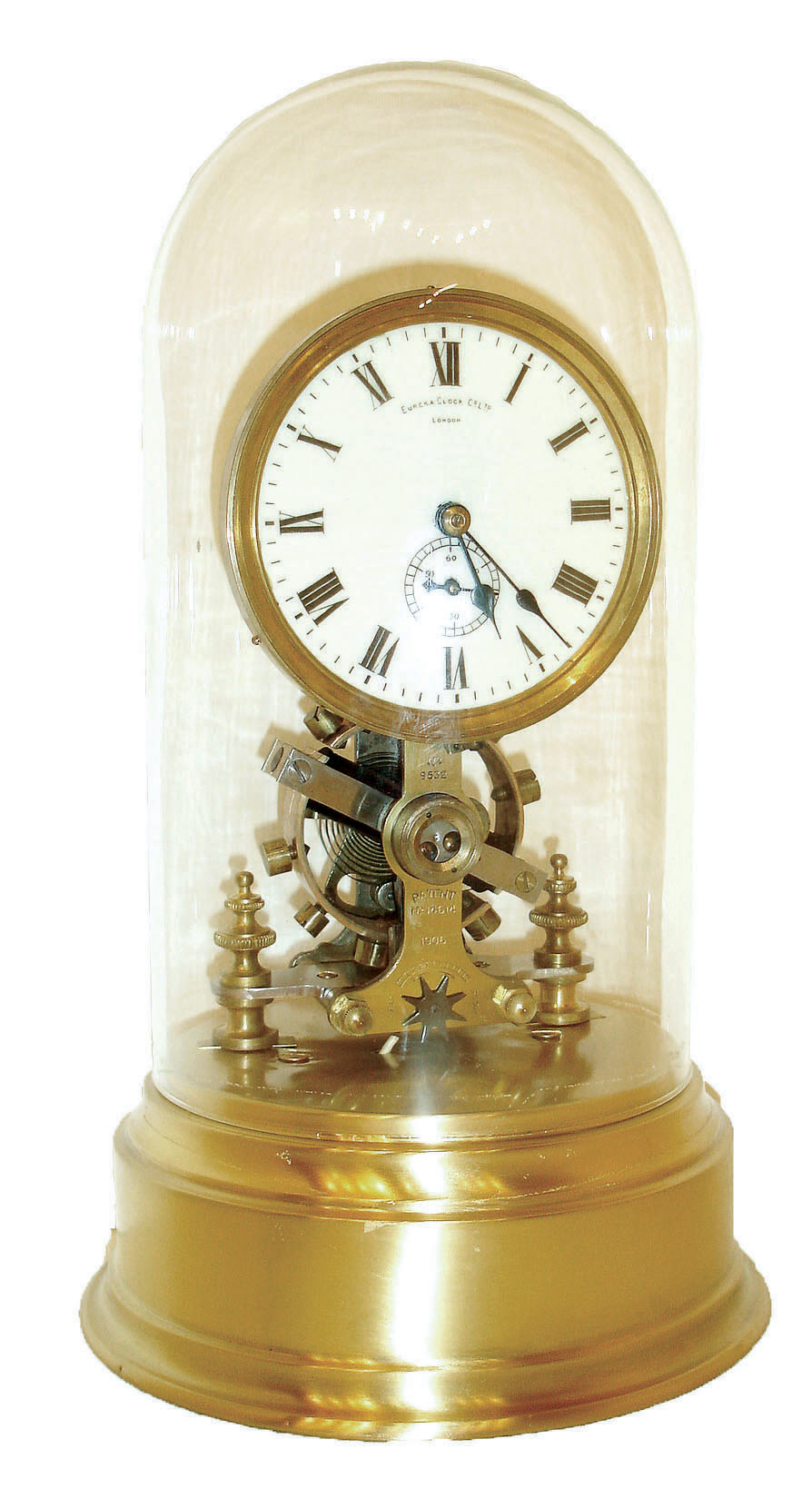 Eureka Clock Co., Ltd., London, England, long running battery clock, the movement with large exposed balance oscillating below the Roman numeral white enamel dial, blued steel hands, all resting on a polished hollow brass base, and covered with a glass dome, serial #9532, c1910 — Antique Clocks Price Guide