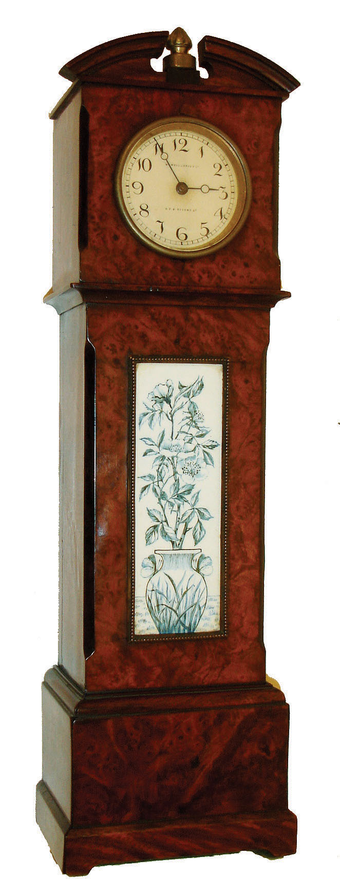 Miniature tall clock, burl walnut veneered case, the trunk with brass framed ceramic panel decorated with a vase and flowers, Arabic numeral painted dial marked "Howell. James & Co. 579 Regent St.", with Imhof 8 day timepiece movement, the clock finial serving as winding crown, c 1910 — Antique Clocks Price Guide