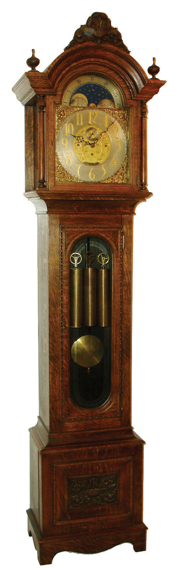 Seth Thomas Clock Co., Thomaston, Conn., tall clock, 8 days, time with quarter chimes on four bells and hour striking on cathedral gong, triple weight driven movement in a quarter sawn carved oak case with beveled trunk door glass and carved and turned full columns flanking hood.  The brass dial has applied cast brass spandrels and engraved dial center, a silvered chapter ring with applied brass numerals and moon phase, c1900 — Antique Clocks Price Guide