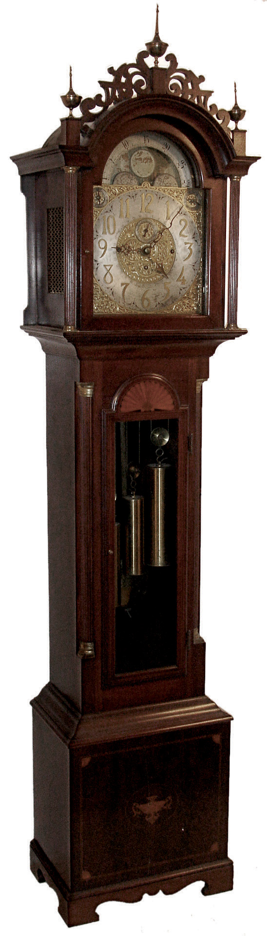 J.J. Elliott, 5 Percival St., London, England, tall case clock, 8 days, time, strike, with calendar and chimes on eight bells and five gongs. Three brass, weight driven movement in a inlaid mahogany case with fluted corner columns with brass capitals. Fretwork crest with three brass finials, inlaid herring bone, fan and urn elements. The brass dial has a silvered chapter ring, engraved and pierced brass spandrels and elaborate dial center, moon phase, subsidiary seconds, strike / silent and tune selectors for Whittington & Westminster, c1915 — Antique Clocks Price Guide
