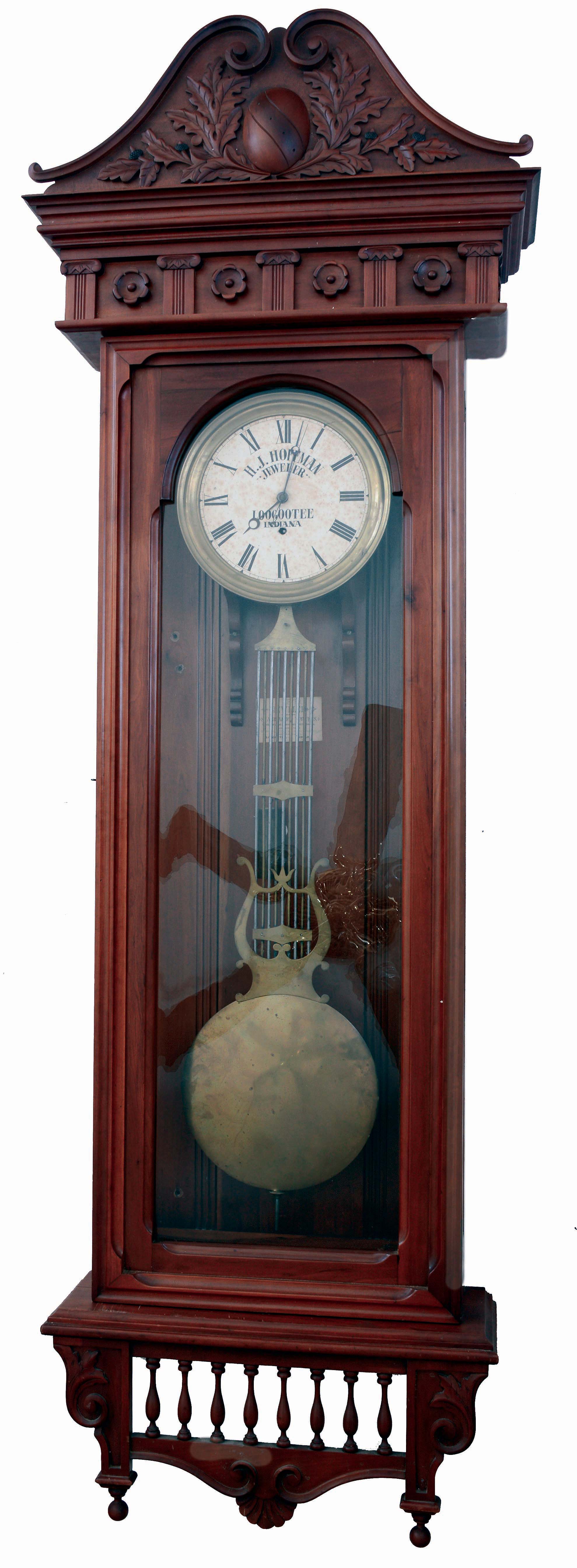 Jewelers hanging regulator, large custom made cherry case with glazed front and sides, molded cornice and scroll carved, oak leaf and acorn decorated top above a frieze with applied turned and carved ornament, the case bottom with leaf carved corbels flanking a balustrade with scroll and scallop carved drop, Roman numeral paper dial marked "H.J. Hoffman Jeweler Loogootee Indiana", blued steel Breguet style hands and with center seconds hand, Swiss weight driven, 8 day timepiece movement with pinwheel escapement, brass clad weight, gridiron pendulum with lyre ornament and large brass clad ball, interior of case with a photo of the shop of J. Meyer Jeweler, Loogootee, Indiana, and also his trade card, c1880 — Antique Clocks Price Guide