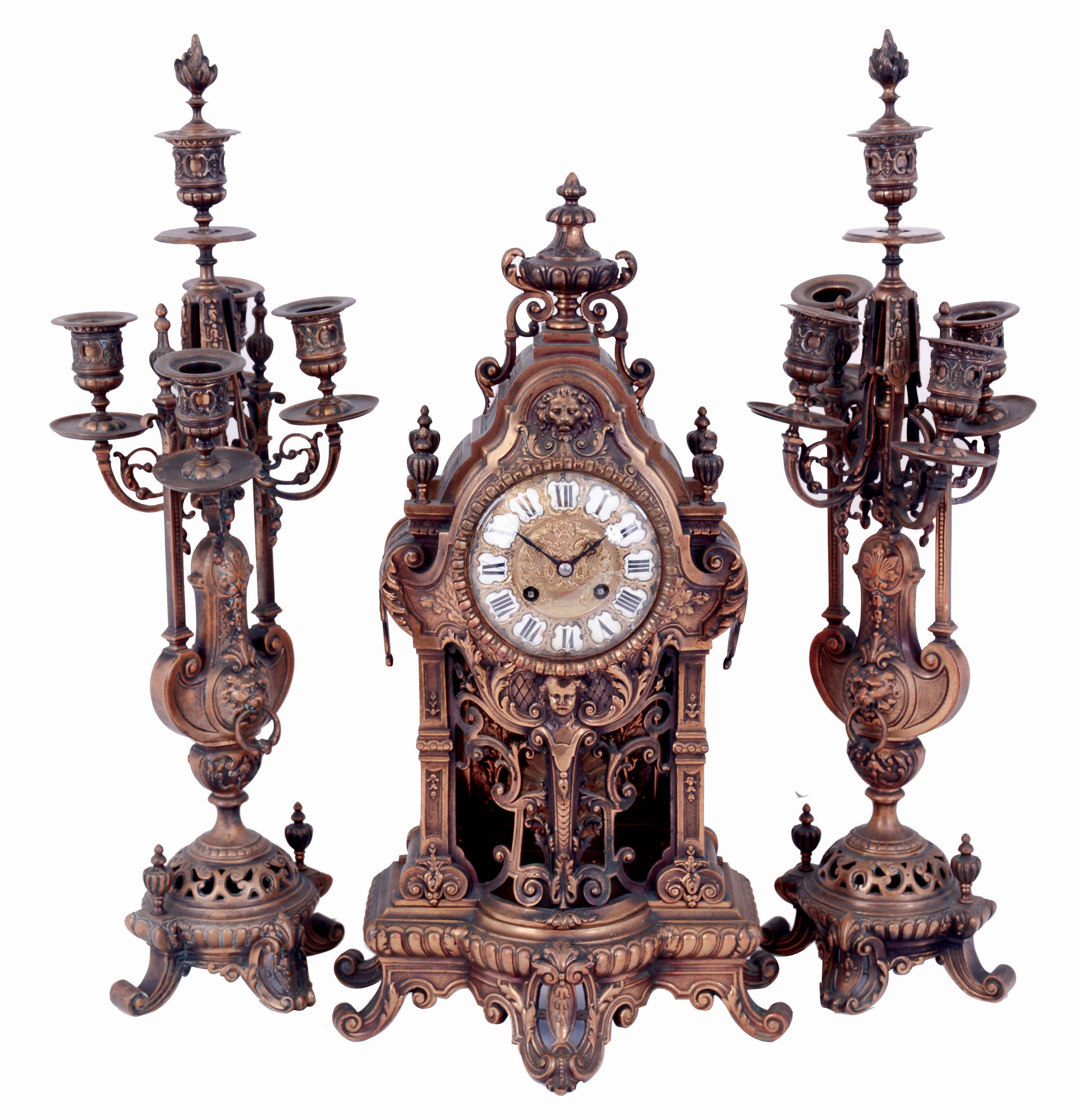 France, three piece mantel garniture showing renaissance revival influence, the bronze clock case with gadrooned base on scroll feet, openwork center section with central caryatid, foliate ornament, and pilasters, the case top with lion mask, finials, and surmounted by a gadrooned urn, brass repousse dial with Roman numeral, white enamel cartouches, 8 days, time and strike movement with Helios mask pendulum, with a pair of candelabra matching the clock, c1880 — Antique Clocks Price Guide