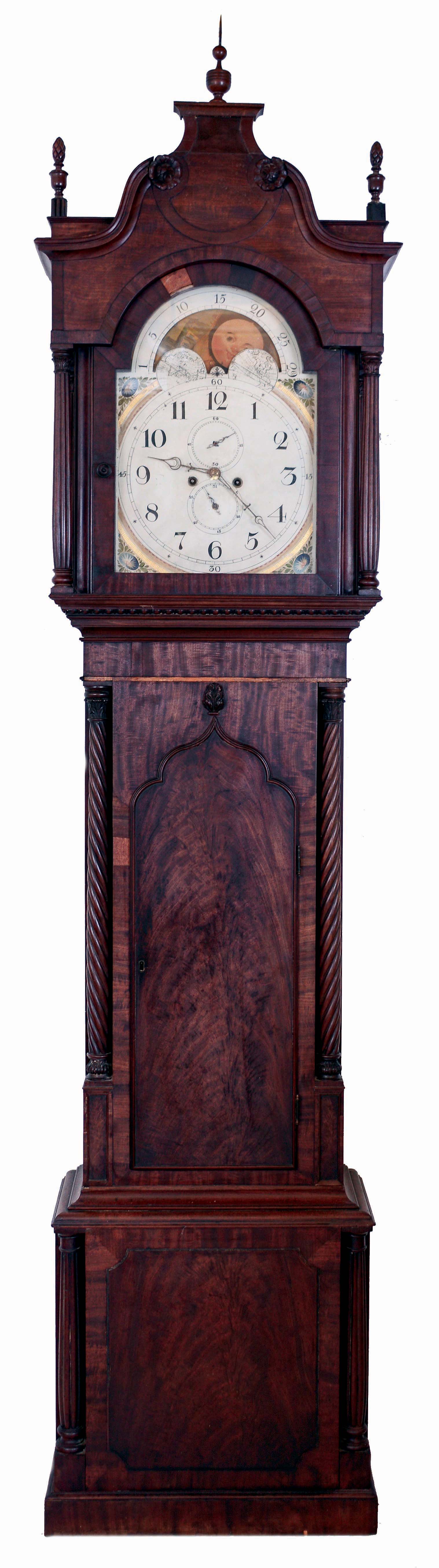 English tall clock, 8 days, time and strike, on gong, weight driven movement in a mahogany and crotch mahogany veneer case with reeded columns flanking hood and base plinth, and rope turned columns flanking trunk, flame finials on hood with carved rosettes on goose neck crest and Gothic arched crotch mahogany trunk door. The painted iron dial has moon phase, date calendar and painted morning glory spandrels, c1840 — Antique Clocks Price Guide