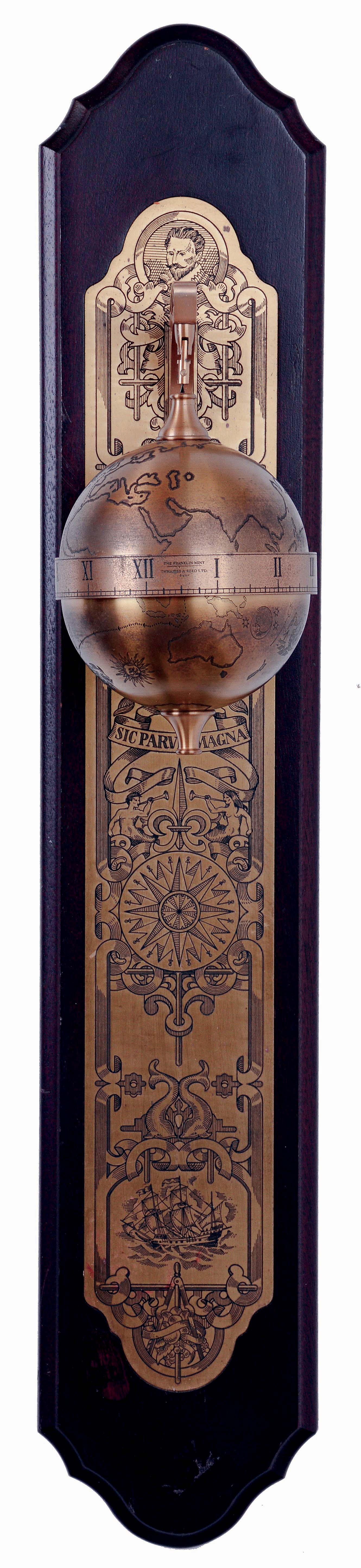 Thwaites & Reed, England for the Franklin Mint, Sir Francis Drake model falling ball gravity clock. The spherical, weighted, engraved brass case containing the 8 day timepiece movement, and with annular time display, suspended from a bracket affixed to a wall mounted board, with engraved ornamental brass back plate, c1980 — Antique Clocks Price Guide