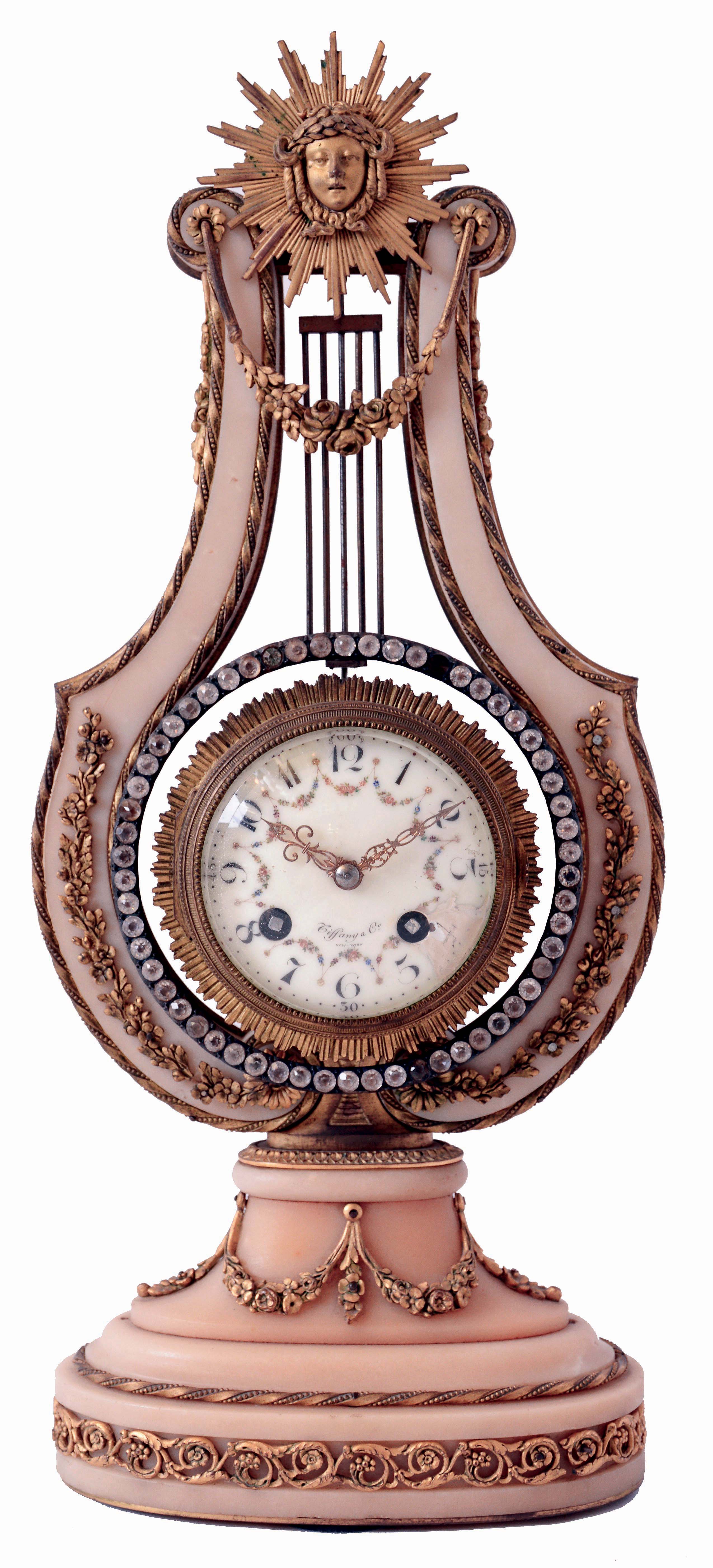 France, for Tiffany & Co., New York, lyre form mantel clock, white marble case decorated with gilt bronze ornament including floral festoons and other foliate ornament, the top with Helios mask, the pendulum suspended behind mask and with oscillating ring of brilliants, Arabic numeral white enamel dial, 8 days, time and strike pendule a Paris movement, dial and movement signed, c1900 — Antique Clocks Price Guide
