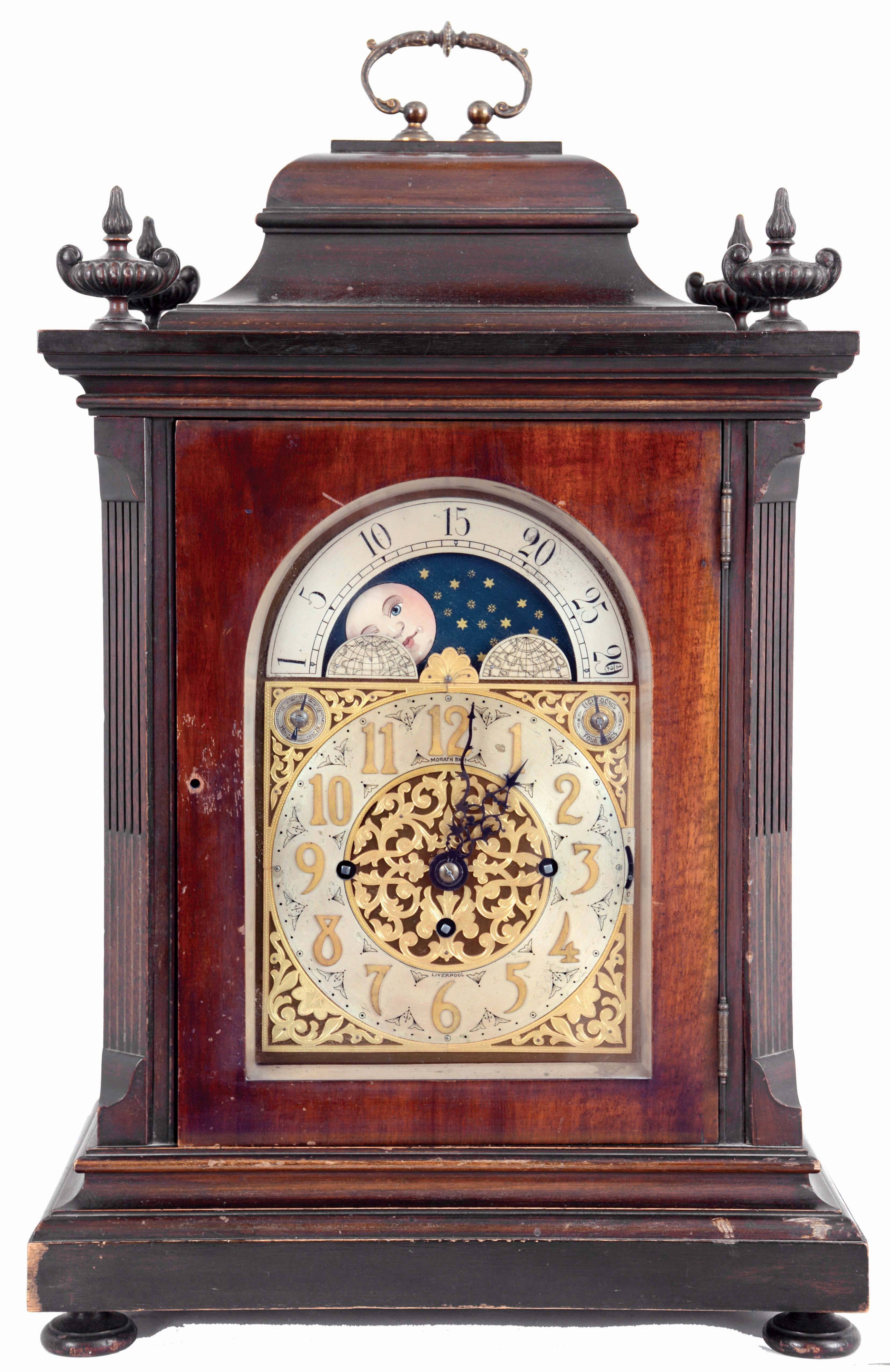 Winterhalder & Hofmeier, Germany, for Morath Brothers, Liverpool, England, 3 train bracket clock. The mahogany case has a heavily molded base and top, stop fluted pilasters and carved urn finials, the doors and sides with thick, beveled glasses, signed composite dial with Arabic numeral silvered chapter ring, gilt spandrels and center, and with moon phase display in the arch, 8 days fusee movement chiming at the quarters on four or eight gongs, and counting the hours on a larger gong. Inside of case is a Morath Brothers label dated July, 1918 — Antique Clocks Price Guide