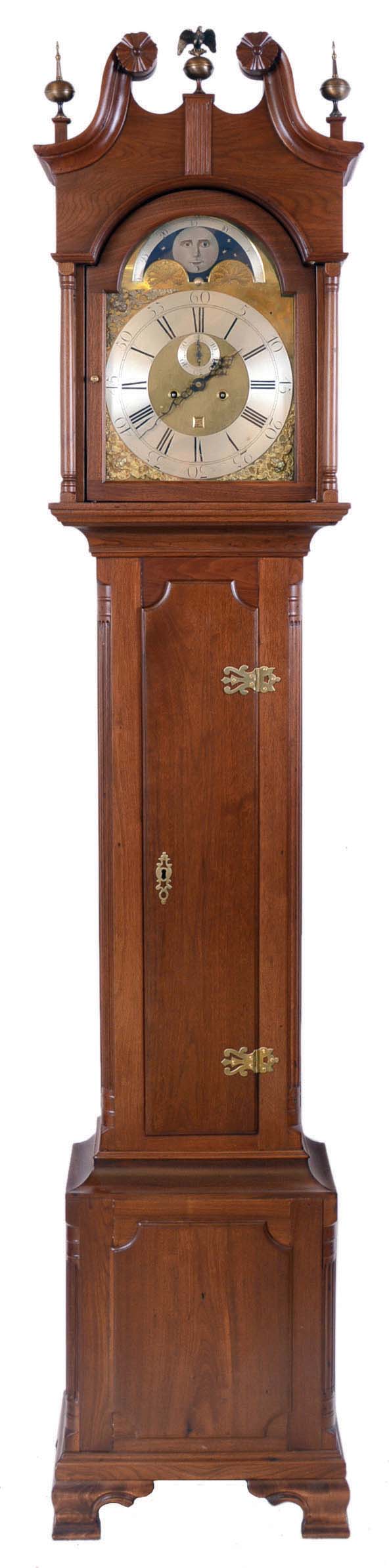 Thomas Kennerdal, Wigan, tall clock, 8 day, time and strike, weight driven English movement, c1770, in a Pennsylvania walnut case with broken arch top, c1795, with applied carved rosettes, four full columns flanking hood, three brass finials, applied panel in base with ogee bracket feet and reeded quarter columns. The brass dial has applied silvered chapter ring, date calendar, cast brass spandrels and moon phase. — Antique Clocks Price Guide