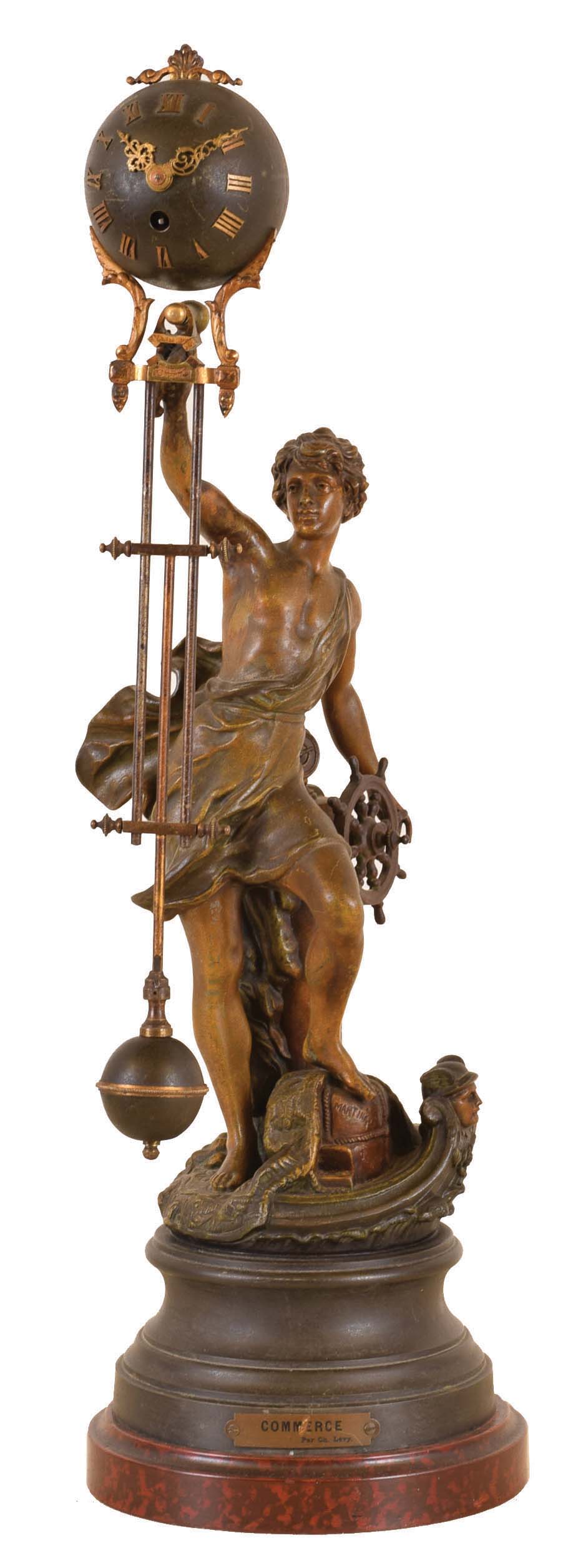 France, swinging clock, the statue representing "Commerce", by Ch. Levy, the standing male figure at a ships wheel, and with a selection of goods at his feet, his right arm held aloft, and supporting the swinging timepiece, the 8 day movement contained in the patinated, upper sphere, with three rod gridiron style connection to matching lower ball, alll mounted to a patinated, molded base, with faux marble plinth — Antique Clocks Price Guide