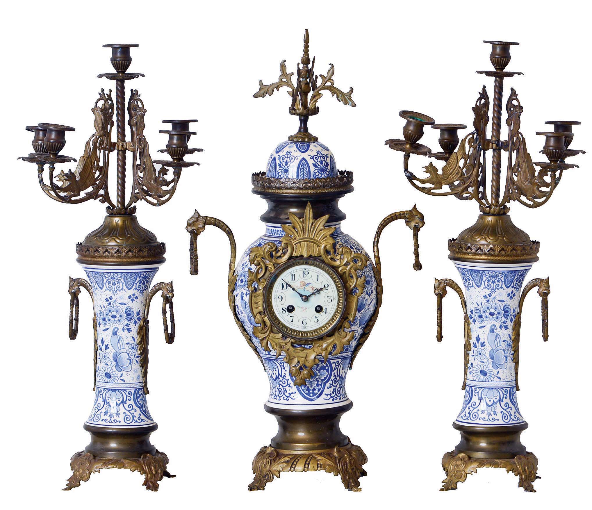 French, Blue and White, Delft style mantel garniture set [3 piece], of brass and china, the candle stands with bronze, winged gargoyles supporting each candle, and with fancy porcelain dial with hand painted cherub below 12 — Antique Clocks Price Guide