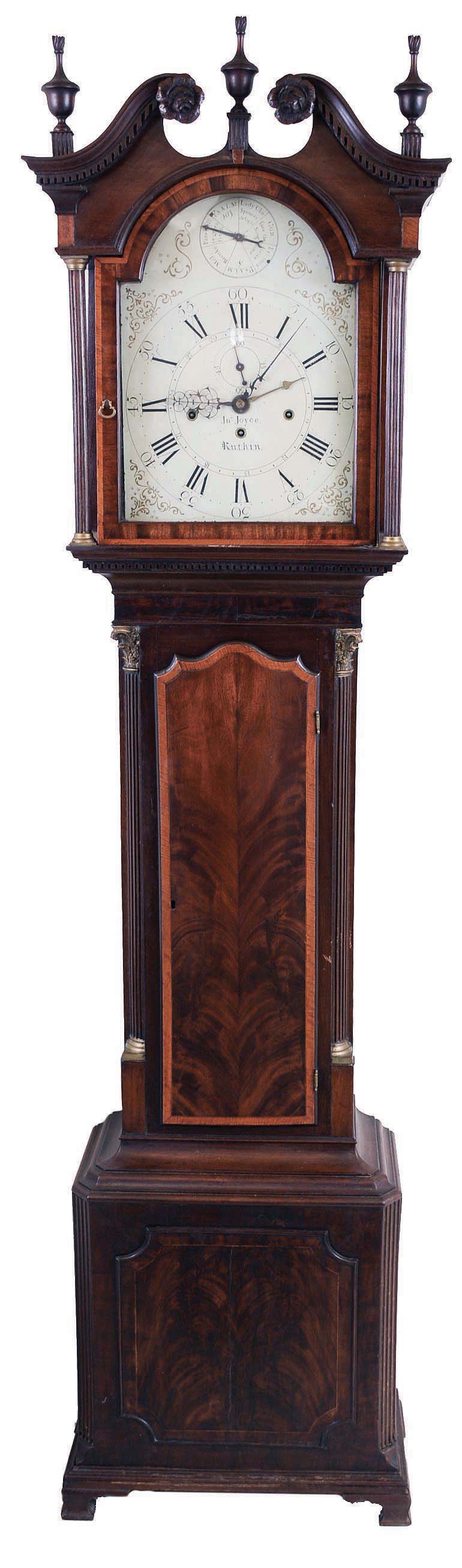 John Joyce, Ruthin, Wales, musical three train tall case clock, 8 days, time, strike and musical weight driven movement playing one of seven tunes (including a hymn on Sunday) every four hours on eight bells and single bell hour strike with painted cast iron pendulum bob. The case is a high styled mahogany veneer case with carved rosettes on broken arch, three carved urn finials with flame tops, dental moldings, fluted columns flanking dial, inlaid banding surrounding doors, fluted quarter columns with brass Corinthian terminals and matched crotch mahogany veneers on trunk with matching raised crotch mahogany panel on base with fluted columns on base resting on ogee bracket feet. The painted metal dial is signed by maker, "John Joyce Ruthin", and has seven tune selector subsidiary dial, sweep center calendar and beautifully pierced hands. — Antique Clocks Price Guide