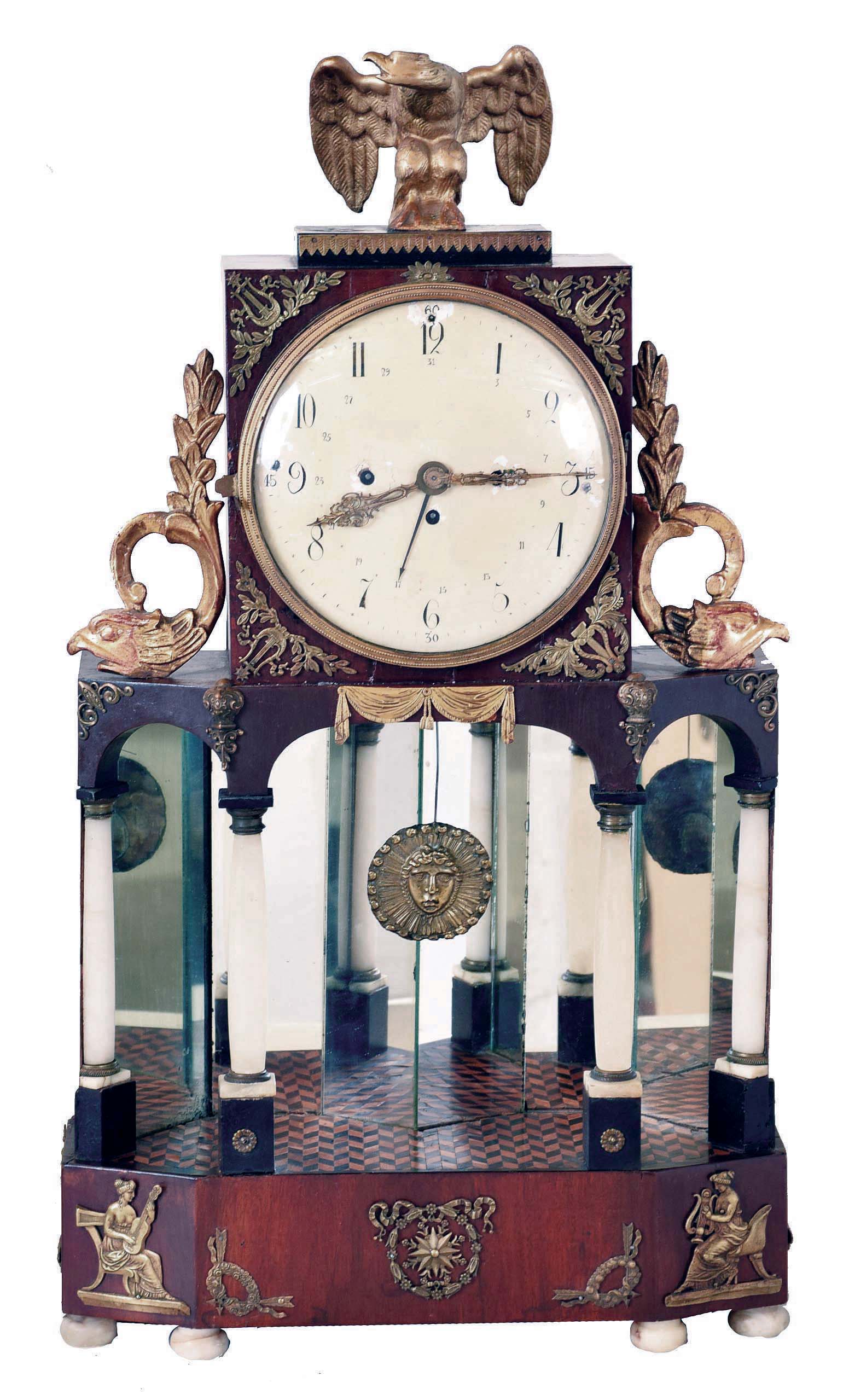 Austria, large neoclassical mantel clock, the mirrored portico base with parquet floor, alabaster columns, and with gilt bronze mounts, with square upper case with flanking dolphins containing the clock, and surmounted by a gilt eagle, Arabic numeral white enamel dial with date indication, very elaborate pierced and engraved gilt hands, two day brass, grand sonnerie striking movement, sounding the hours and quarters on bells, with repousse Helios mask pendulum — Antique Clocks Price Guide