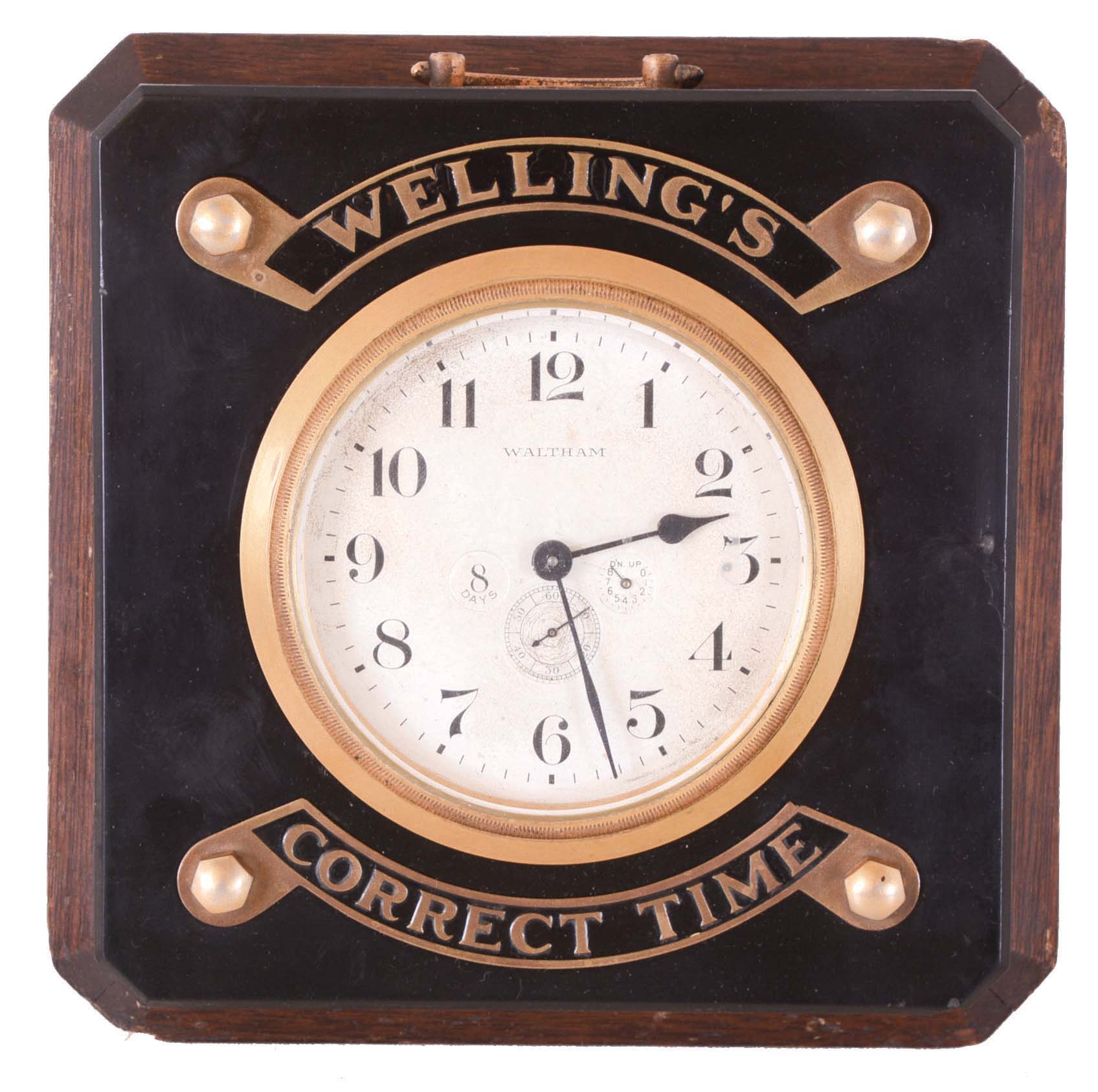 Waltham, "Wellings Correct Time" counter display clock, square, mahogany case with sloping top, black Bakelite top with chamfered edge, mounted with plaques marked "Wellings" and "Correct Time", framing the gilt bezel and silvered, Arabic numeral dial with wind indicator, 8 day timepiece movement — Antique Clocks Price Guide